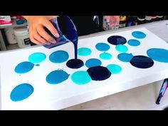 a person is painting circles on a white table with blue and black paint in it