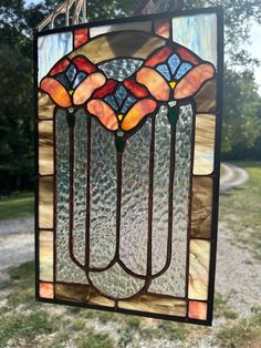 a stained glass window hanging from the side of a tree in front of a dirt road