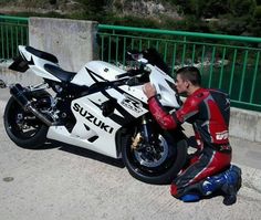 a man in red and black sitting on the ground next to a white motorcycle