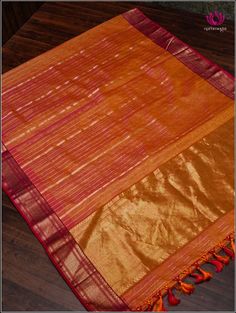 an orange and pink silk saree with tassels on the border, sitting on a wooden floor