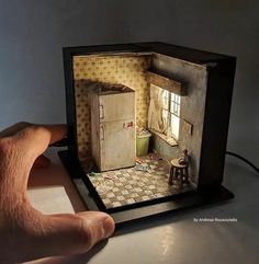 a hand is holding up a miniature model of a doll's house with the door open