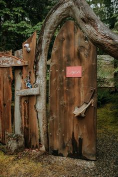 a wooden gate with a sign on it and a tree trunk in the foreground