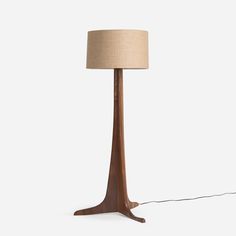 a wooden floor lamp with a beige shade on the base and a light bulb plugged in