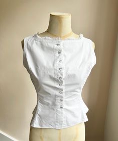 A lovely Edwardian or possibly Victorian corset cover.  Nicely made from crisp, starched white cotton. Great structure and shape.  Trimmed at the top with dainty lace.  Fastens at the front with lots of self-covered buttons.  Shown on a UK size 8 (a little big on the bust.) Highly wearable.  Freshly and carefully laundered.  Measurements are taken when laid flat: For a rough guide, the best fit is XS-S.  Waist- up to 26 inches  Across the back- 17 inches approx.  Centre back to hem- 18 inches  C Fitted Victorian Cotton Blouse, Victorian Cotton Fitted Blouse, Fitted Camisole Blouse For Daywear, Victorian Fitted Tops For Summer, Fitted Victorian Summer Tops, Fitted Victorian Tops For Summer, Victorian White Cotton Top, Victorian Style White Cotton Top, Fitted Cotton Camisole Blouse