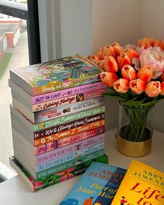 a stack of books sitting on top of a table next to a vase filled with flowers