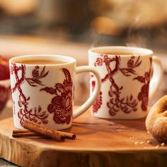 two coffee mugs sitting on top of a wooden cutting board next to cinnamon sticks