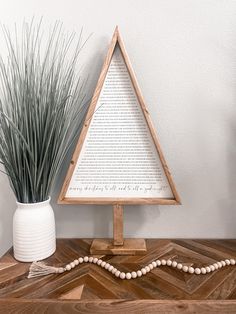 a small wooden christmas tree sitting on top of a table next to a white vase