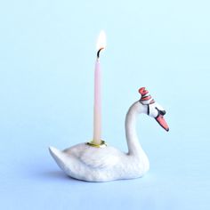 a white swan with a candle in it's beak sitting on a blue surface