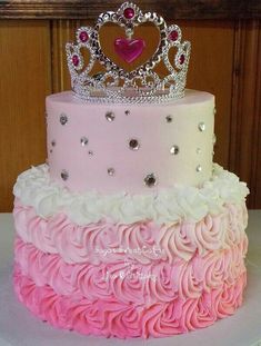 a three tiered cake decorated with pink and white frosting, topped with a tiara