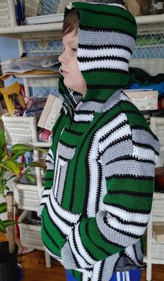 a young boy wearing a green and white striped sweater standing next to a potted plant