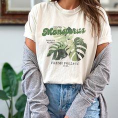 Spruce up your wardrobe with this vibrant rooted Monstera plant Comfort Colors T-shirt, perfect for any plant lover! Featuring a charming indoor plant graphic, this gardening shirt is an ideal gift for greenhouse enthusiasts and indoor plant aficionados. Get ready to bloom in style with this cozy, plant-themed tee! -The Comfort Colors 1717 tee is made with medium fabric (6.1 oz/yd² (206.8 g/m consisting of high quality, 100% ring-spun US cotton for long-lasting comfort. -The relaxed fit keeps th Casual Green Tops With Plant Print, Spring Relaxed Fit T-shirt With Plant Details, Green Graphic Tee With Plants Print, Green Graphic Tee With Plant Print, Casual Summer Tops With Plant Details, Green Relaxed Fit T-shirt With Plant Detail, Botanical Green Tops With Plant Print, Casual Leaf Print Relaxed Top, Green Botanical Print Tops