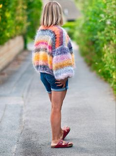 a woman is walking down the road wearing a colorful sweater and denim cut off shorts