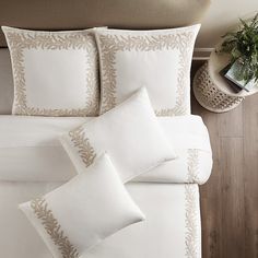 a bed with white sheets and pillows on top of it next to a potted plant