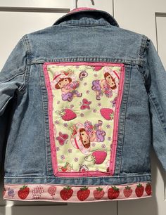 a denim jacket with strawberry patchwork on the back and pink trimmings, hanging from a hook