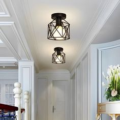 two lights are hanging from the ceiling in a hallway with white walls and wood flooring