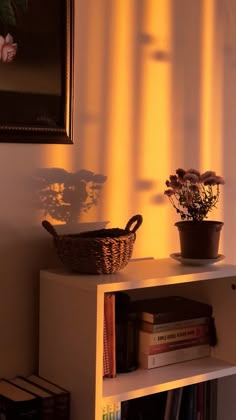 a shelf with books and flowers on it next to a framed painting in the corner