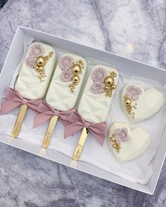 four decorated cakes in a white box on a marble counter top with gold handles and pink bows