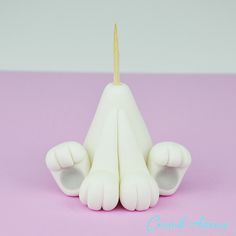 a white cat shaped candle sitting on top of a pink surface with a toothpick sticking out of it's mouth