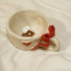 a white ceramic bowl with red handles and two hearts on the inside, sitting on a white sheet