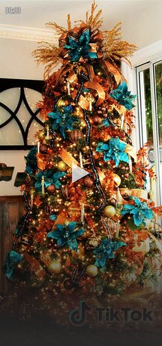 a decorated christmas tree with blue, gold and orange ornaments on it in front of a window