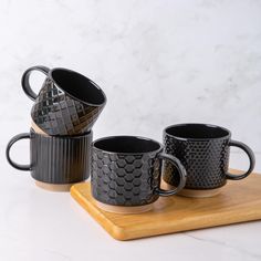 three black coffee mugs sitting on top of a wooden tray next to each other