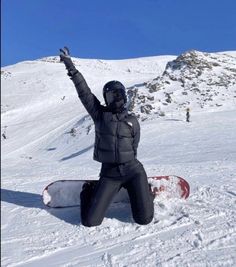 a person sitting in the snow on top of a snowboard with their arms up