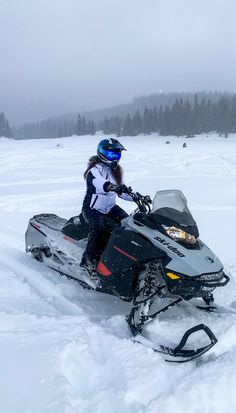 a woman riding on the back of a snowmobile down a snow covered slope with trees in the background