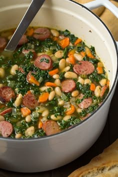 a pot full of soup with sausage, beans and spinach in it next to some pita bread