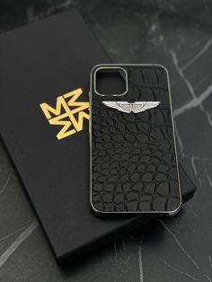 an iphone case sitting on top of a black book next to a gold logo sticker