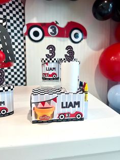 a table topped with boxes filled with food next to red and black balloons in the shape of cars