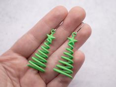 a pair of green christmas tree earrings in the palm of someone's left hand