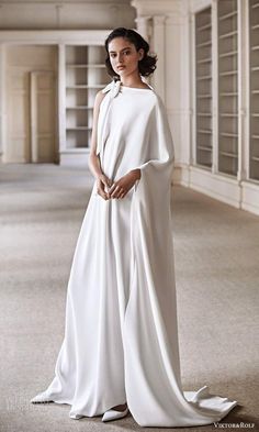 a woman wearing a white gown and cape standing in an empty room with bookshelves