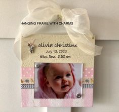 a hanging frame with a baby's photo and ribbon on the front of it