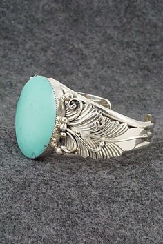 This stunning turquoise and sterling silver bracelet was made by Navajo silversmith Gilbert Smith. The back is partially signed RB and .925.Size: 5 3/8" (will fit up to a 6 3/8" wrist)Gap: 1"Width: 1 3/8"Cuff Width: 1/2"Free shipping on all orders! We ship with USPS and always include tracking. All orders ship within a day of payment.Returns are accepted up to 30 days after you receive your order. Just send us a message. Our shop offers cash back or store credit. The item must be returned in new Elegant Turquoise Bracelet With Inlay, Elegant Turquoise Inlay Bracelet, Elegant Sterling Silver Bracelet With Turquoise, Elegant Turquoise Engraved Sterling Silver Bracelet, Elegant Engraved Turquoise Sterling Silver Bracelet, Elegant Turquoise Oval Sterling Silver Bracelet, Southwestern Turquoise Bracelet With Polished Finish, Southwestern Turquoise Bracelets With Polished Finish, Sterling Silver Bracelet