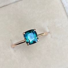 a ring with an emerald colored stone in it sitting on a white cloth covered surface