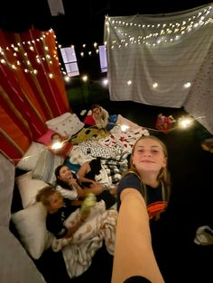 a group of people laying on top of a bed covered in blankets next to string lights