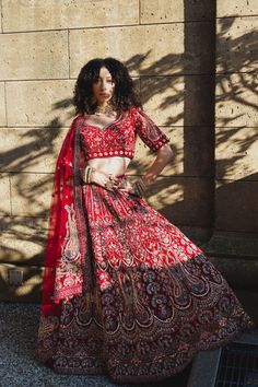 a woman in a red and gold dress standing next to a brick wall with her hands on her hips