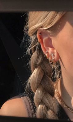 a woman with long blonde hair wearing gold earrings and a braid in her left ear