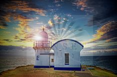 a lighthouse with the sun shining behind it on top of a hill next to the ocean