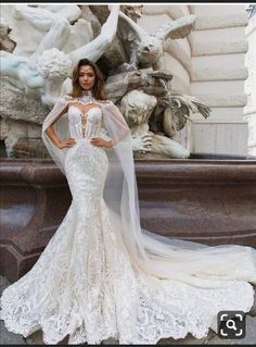 a woman in a white wedding dress standing next to a fountain wearing a long veil