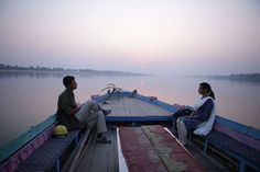 two people sitting on the back of a boat in the middle of water at sunset