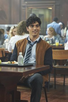 a young man sitting at a table in a restaurant with other people eating and drinking