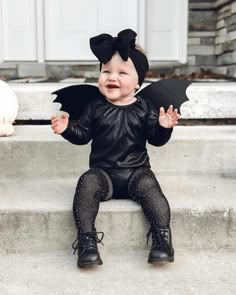 a baby dressed up as a bat sitting on steps