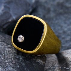 a black and gold ring with a diamond in the center on top of a rock