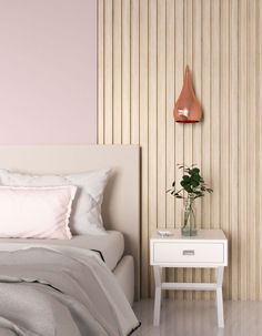 a white bed sitting next to a nightstand with a plant on it and a pink wall behind it