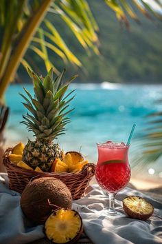 a pineapple drink sits next to some fruit on a towel near the water's edge