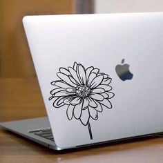 an apple laptop computer sitting on top of a wooden table with a flower decal