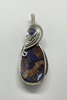 This Boulder Opal Pendant is an exquisite piece featuring a vibrant Boulder Opal beautifully wrapped in Sterling Silver (.925). The addition of a stunning Tanzanite accent enhances the piece, adding a touch of luxury and contrast. The interplay between the opal’s iridescent colors and the rich blue of the tanzanite makes this pendant a captivating and elegant accessory. Approximately 2" long and 13/16" wide. Australian Boulder opals are the second most valuable type of opal (following black opal Unique Iridescent Opal Jewelry, Elegant Iridescent Oval Pendant Jewelry, Elegant Iridescent Wire Wrapped Jewelry, Silver Opal Fusion Jewelry, Unique Opal Wire Wrapped Jewelry, Artisan Iridescent Gemstone Jewelry, Artisan Silver Opal Jewelry, Boulder Opal Pendant, Types Of Opals