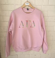 "Alpha Gamma Delta Greek Letter Sweatshirt The letters are 4-4.5\" depending on the size of the sweatshirt.   Letters are completely embroidered in floral font in pastels.  All embroidery is stabilized and has a soft cover fabric backing the embroidery to be soft against the skin.  Sweatshirt letters will look exactly as shown in the same colors.  ~~Sweatshirts used are Gildan Heavy Blend in Pink 8 oz./yd² (US) 13.3 oz./L yd (CA), 50/50 cotton/polyester, 20 singles Classic fit Air jet yarn for s Spring Sorority Long Sleeve Tops, Sorority Long-sleeve Cotton Sweatshirt, Cotton Sorority Sweatshirt With Long Sleeves, Spring Sorority Long Sleeve Sweatshirt, Cotton Long Sleeve Sorority Sweatshirt, Pink Embroidered Tops For College, Sorority Long Sleeve Relaxed Fit Tops, Spring Sorority Sweatshirt With Letter Print, Sorority Sweatshirt With Letter Print In Relaxed Fit