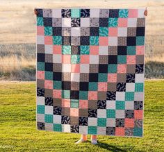 a woman standing in the grass holding up a quilt